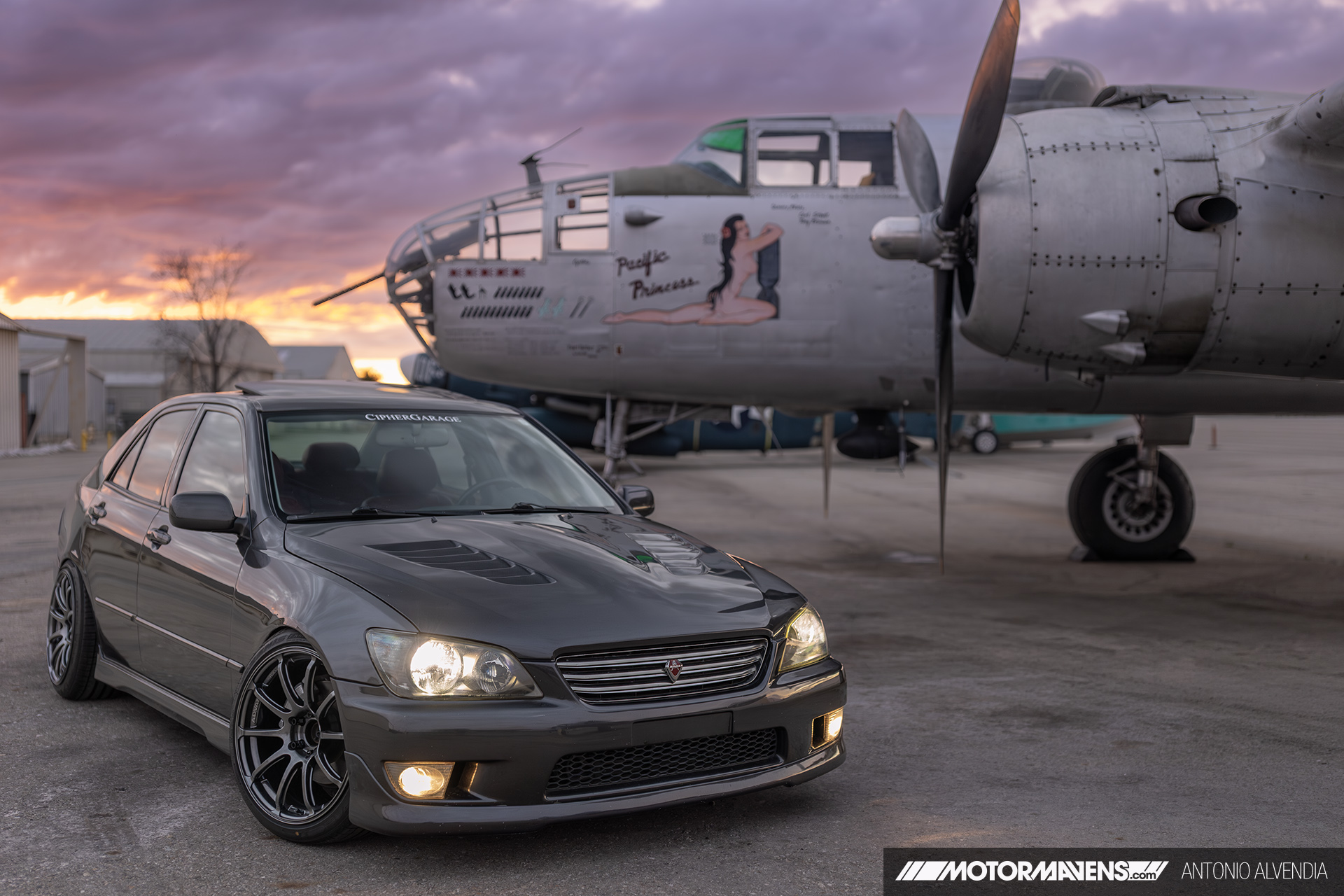 Lexus IS300 with Advan RSII wheels and Chargespeed vented CF hood parked in front of Pacific Princess B25 bomber Doolittle Raid aircraft at airport hangar